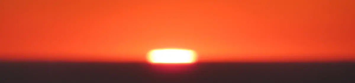 Abstract sunset. A blurry photo depicting a yellow lozenge nestled between a gradient of orange and a fuzzy darkness. Own work, 2023.