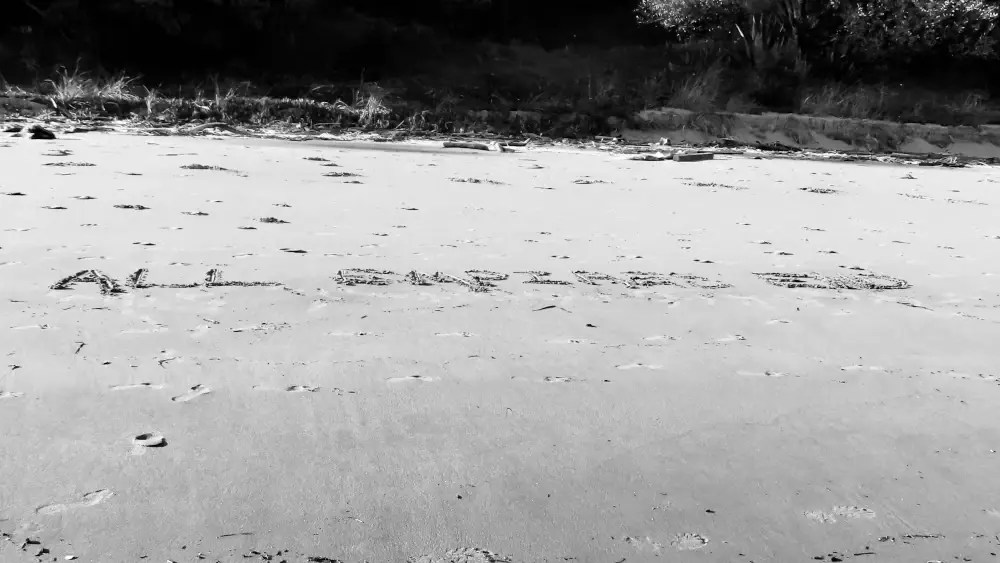 Black and white photo of a beach with All Empires End written in the sand
