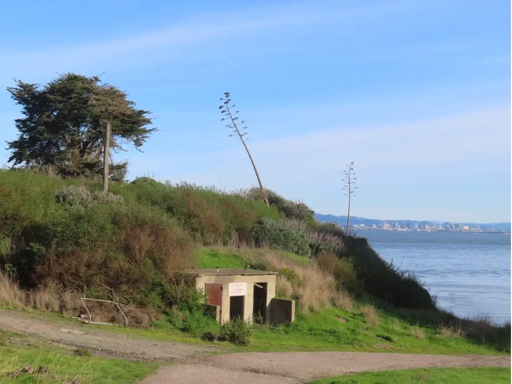A bunker like outbuilding in a hillside with a road leading down to the ocean next to it 
