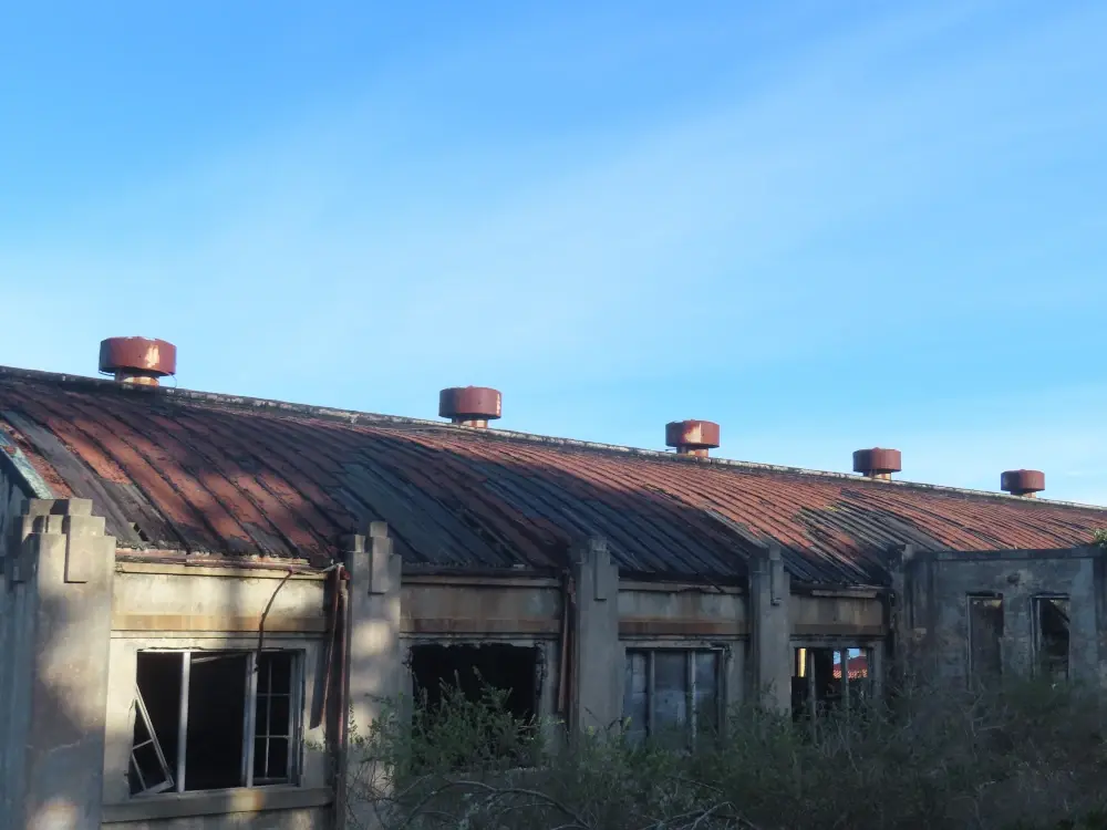The red roof of a large empty building with round vents against a blue sky