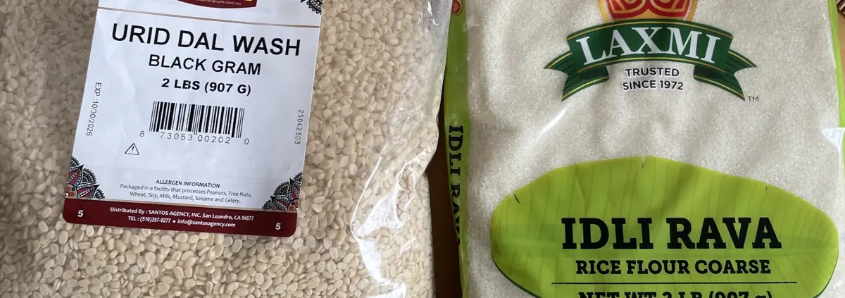 A close crop of two bags of whitish grains, one labelled Urad Dal and the other Idli Rava.