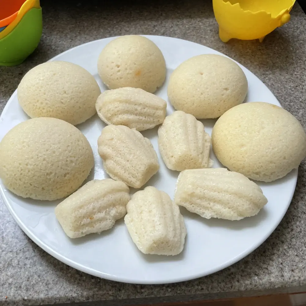 A plate of steamed idli, some of which were steamed in madeline modls and thus shaped like madelines