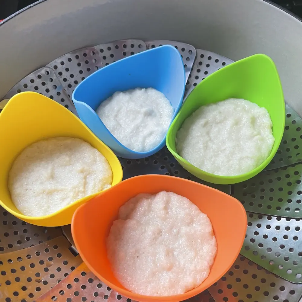 Colorful silicone molds sized for egg poaching are half filled with white batter and sit in a streamer basket