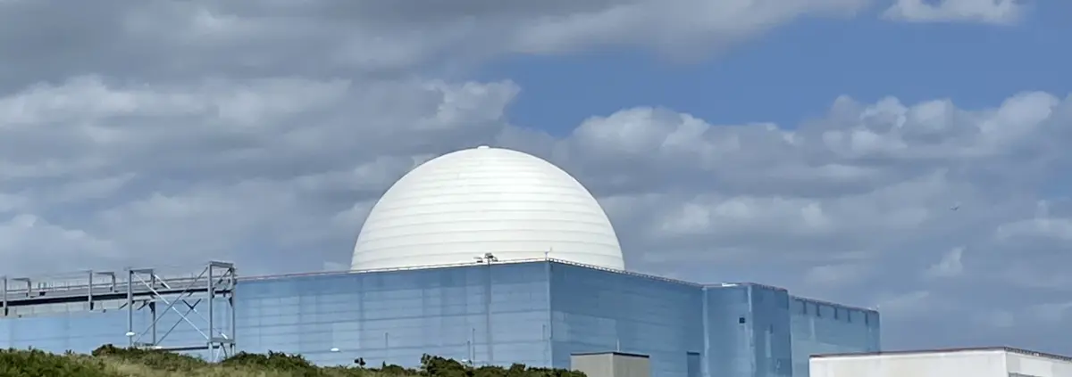 Photo of a white dome rising out of a blue building against a blue sky with fluffy white clouds, the clouds and the sky matching closely the white dome and the blue building. Sizewell B nuclear reactor in Suffolk, England.