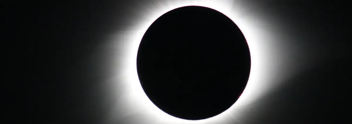 A black hole in a black sky surrounded by a white corona. It is a close crop of a photo of a solar eclipse.