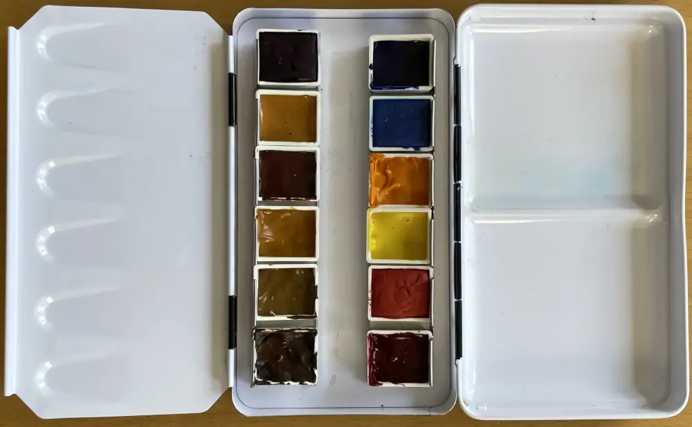 A folding travel palette laid open with filled half-pans of paint in the middle