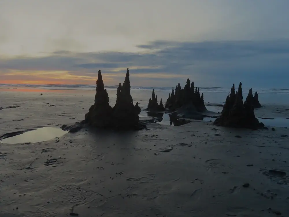 Drippy sandcastle spires against a background of sunset sky look a bit like mysterious spires on a fantasy cover