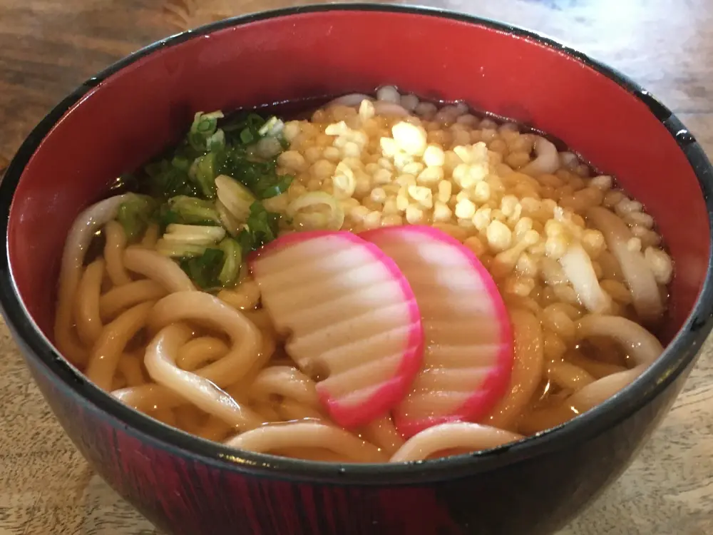 A simple bowl of ramen with two slices of pink fishcake, a modest sprinkle of scallions, and crunchy puffs