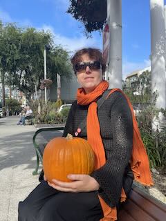 Photo of author holding a pumpkin and wearing a bright orange scarf