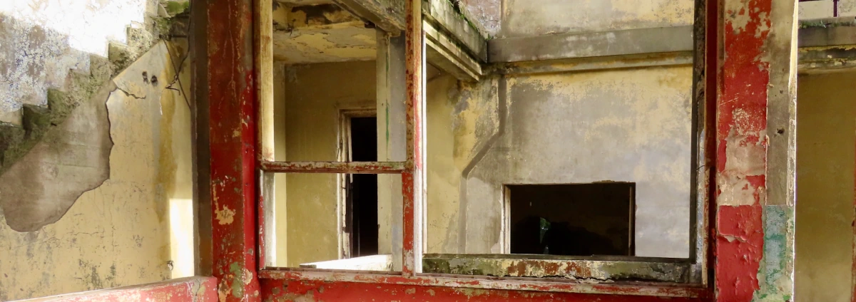 Photo of the exposed insides a decaying building with peeling paint. On the left side of the frame, the peeling cement looks kind of like a monster and someone drew eyes and a smile on it.