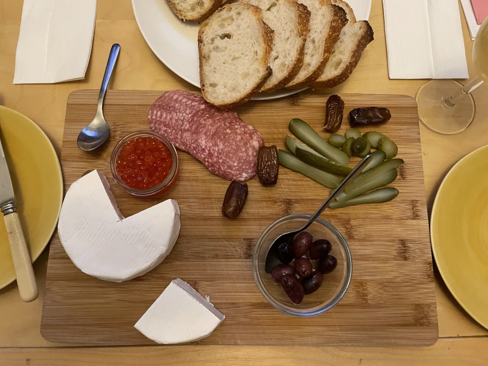 A charcuterie board with brie, caviar, salami, pickles, olives, and dates