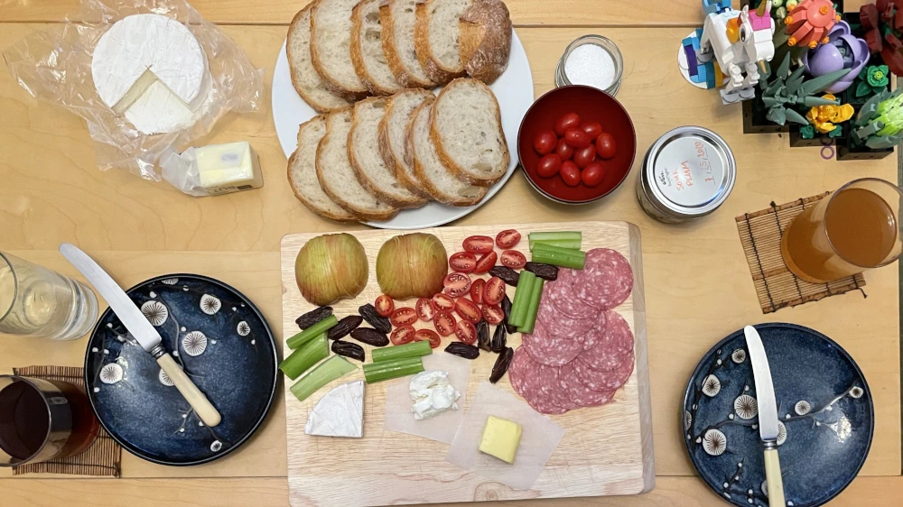 A charcuterie board with brie, goat cheese, butter, salami, celery, tomatoes, sliced apples, and dates