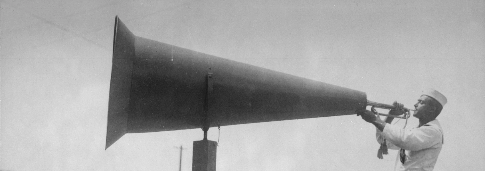 A sailor using a megaphone to increase the loudness of a bugle to wake recruits at U.S.Naval Training Camp, Seattle, Washington in 1947