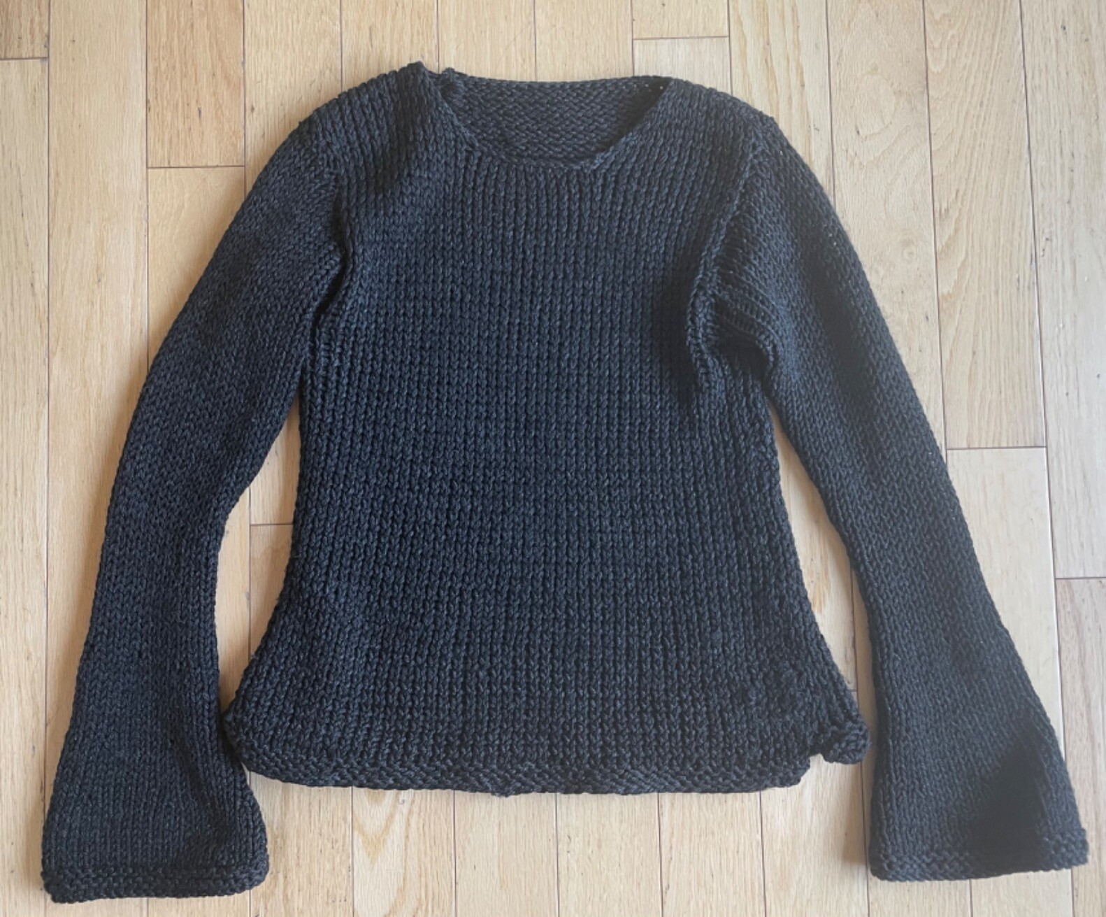 Photo of a hand knit black sweater lying on a light background