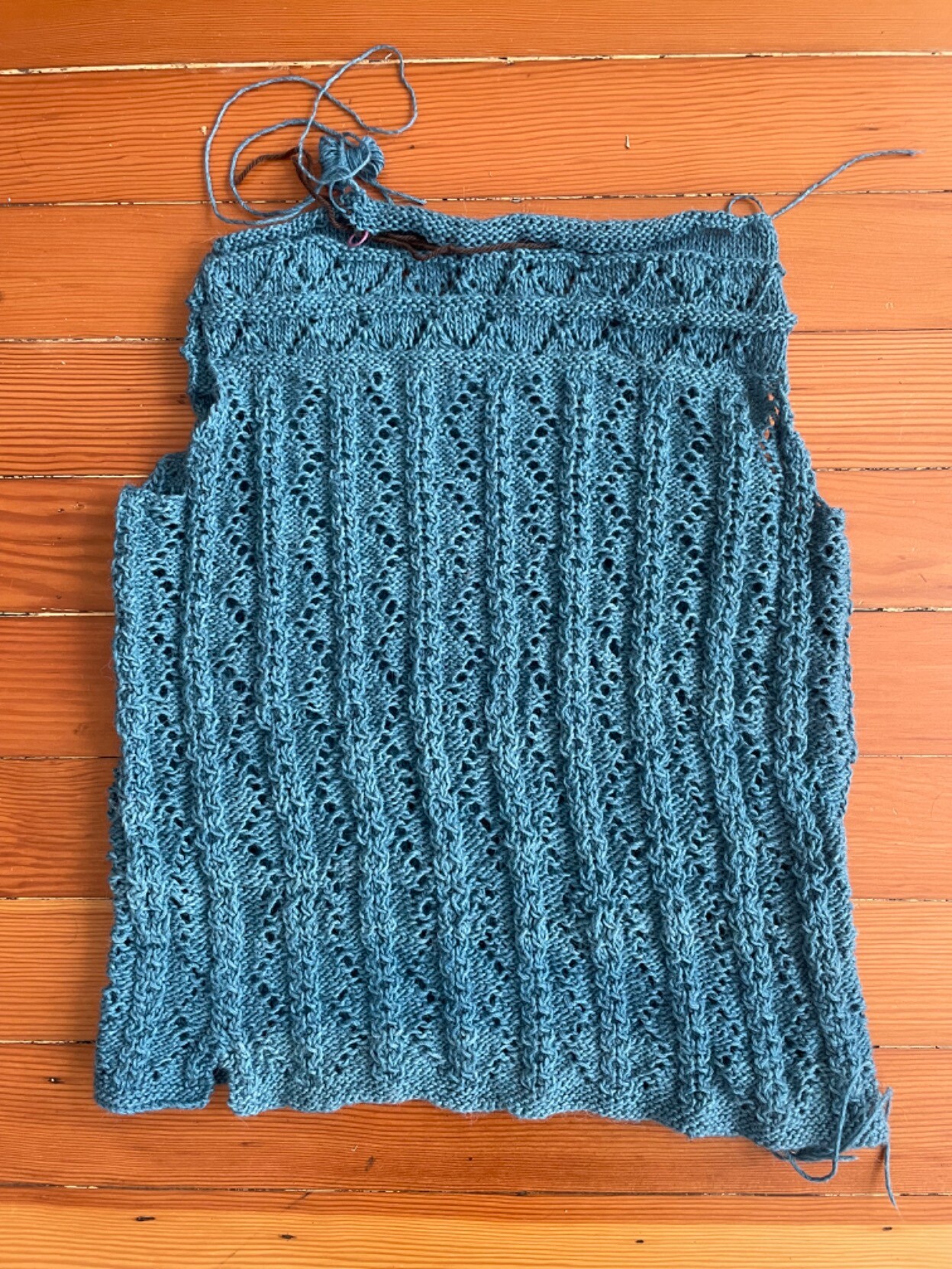 The body of a blue sweater with delicate cables and lace knitting. The sleeves and collar are not yet done.