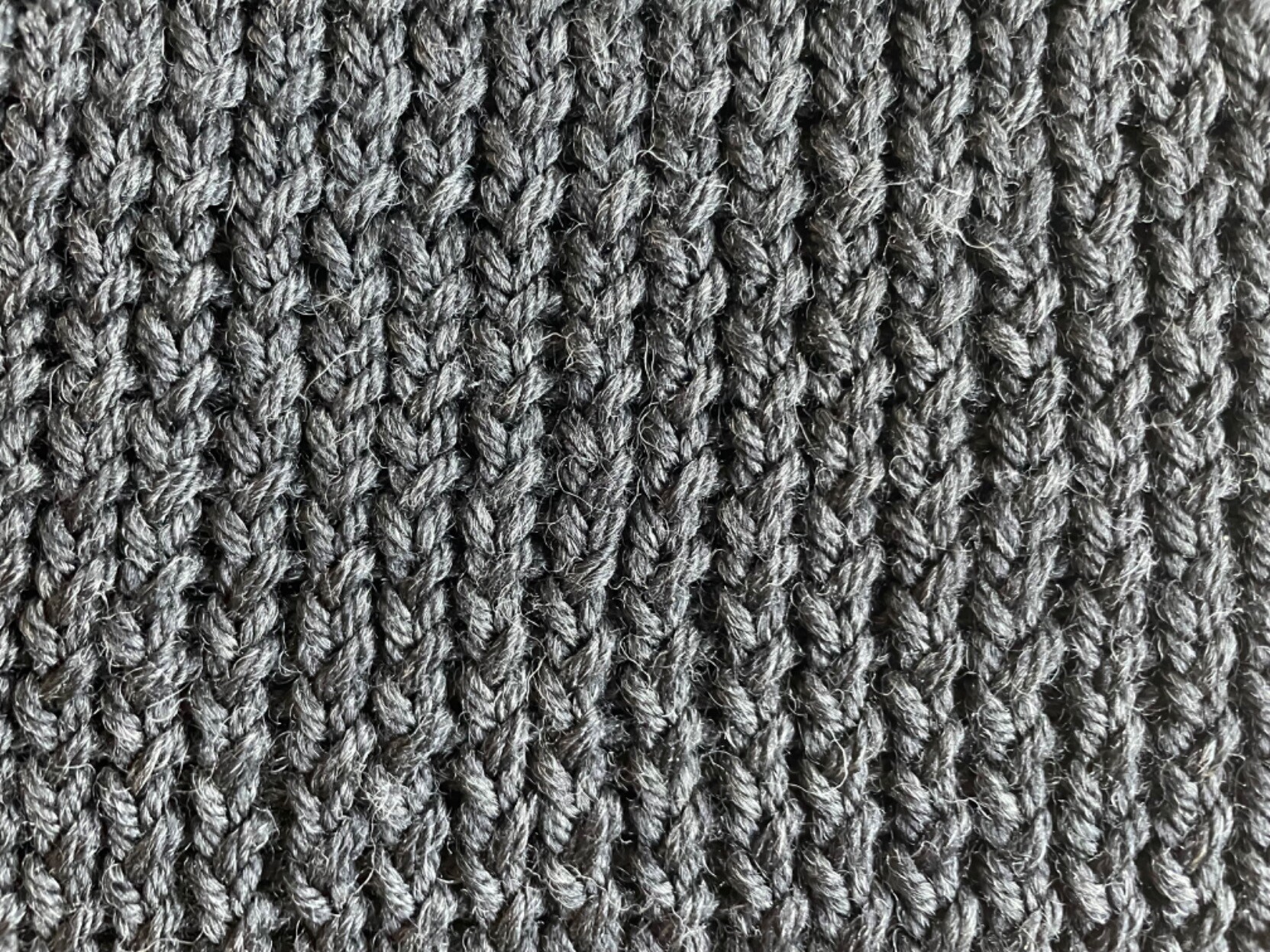 Close up detail of the knit side of fabric in stockinette stitch. The knit stitches are scrunched and twisted.