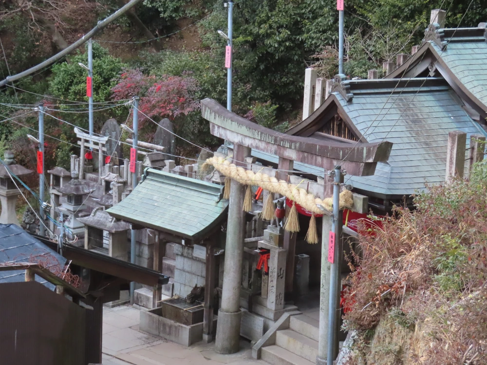 A stone torii in front of an altar has a huge woven rice straw chain