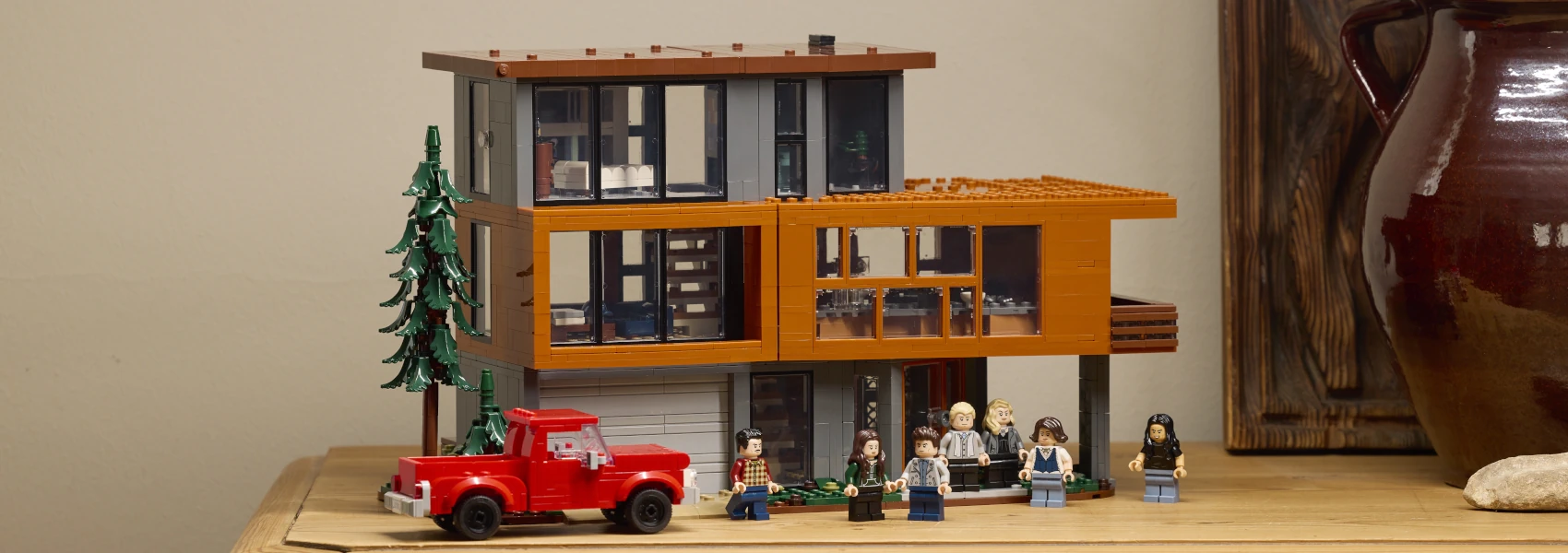 A Lego model of an upscale contemporary house with a red truck parked prominently in front of it and several Lego people figures standing all around. This is the LEGO Ideas Twilight The Cullen House Set.