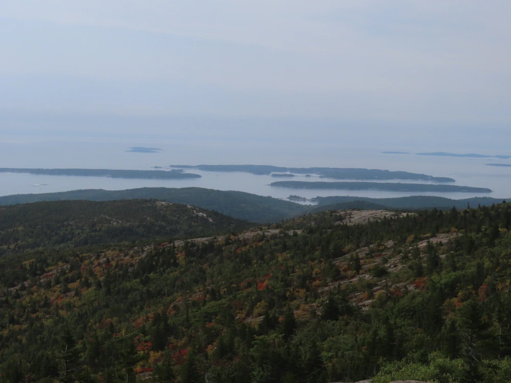 A photo of forested costal islands seen from the top of a mountain. Sky and sea blend.