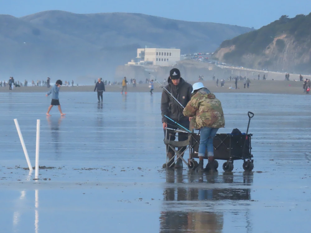 Two people packing up their fishing gear into a rolling cart. They are not wearing waders.