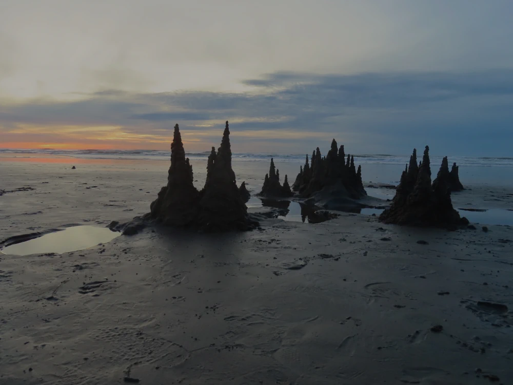 Drippy sandcastle spires against a background of sunset sky look a bit like mysterious spires on a fantasy cover