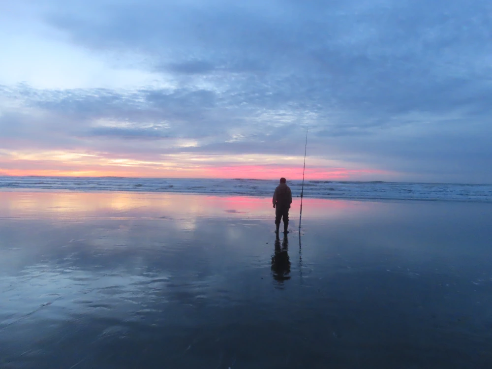 A fisherman stands silhouetted against the brilliant colors of sunset