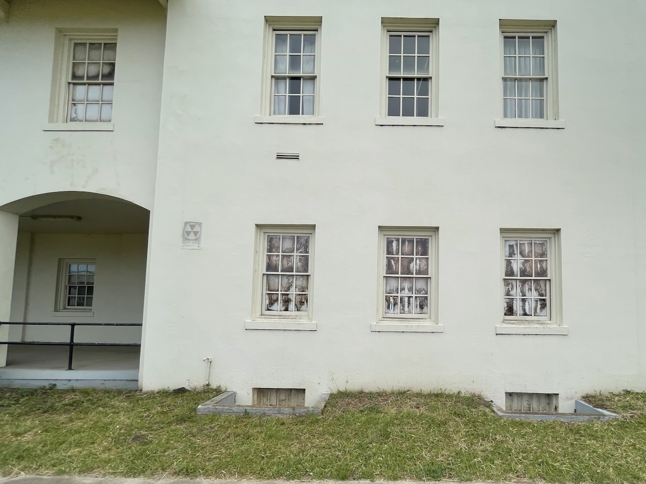 The front of a building with decaying windows and a faded fallout shelter sign