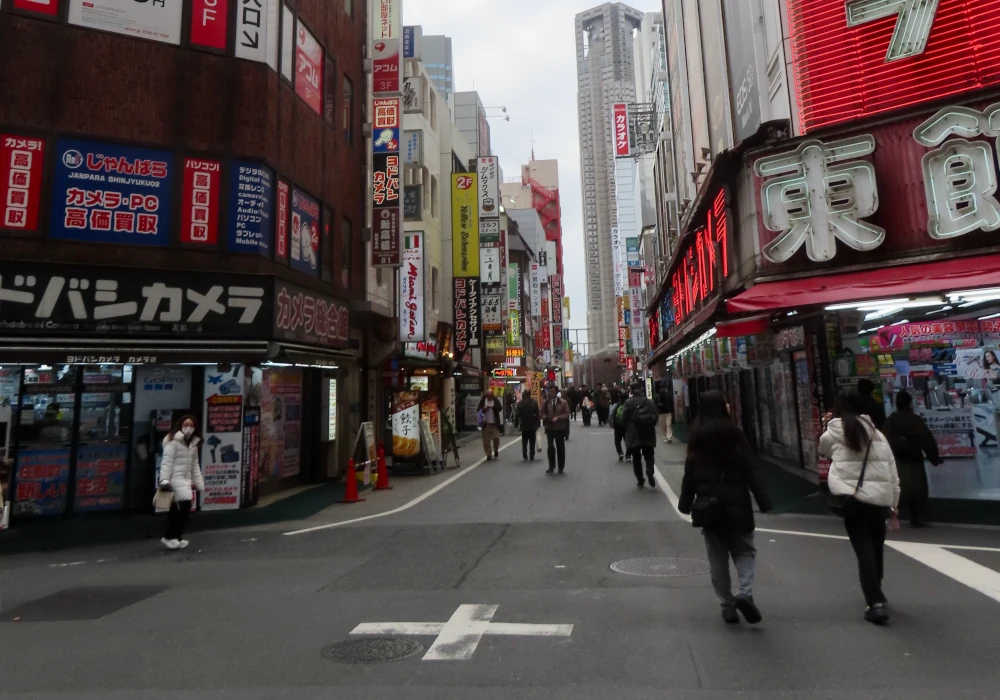 A small street in Tokyo with people walking in the road, lit up store fronts on either side, and sign after sign stretching as far as the eye can see until you get high rises in the horizon