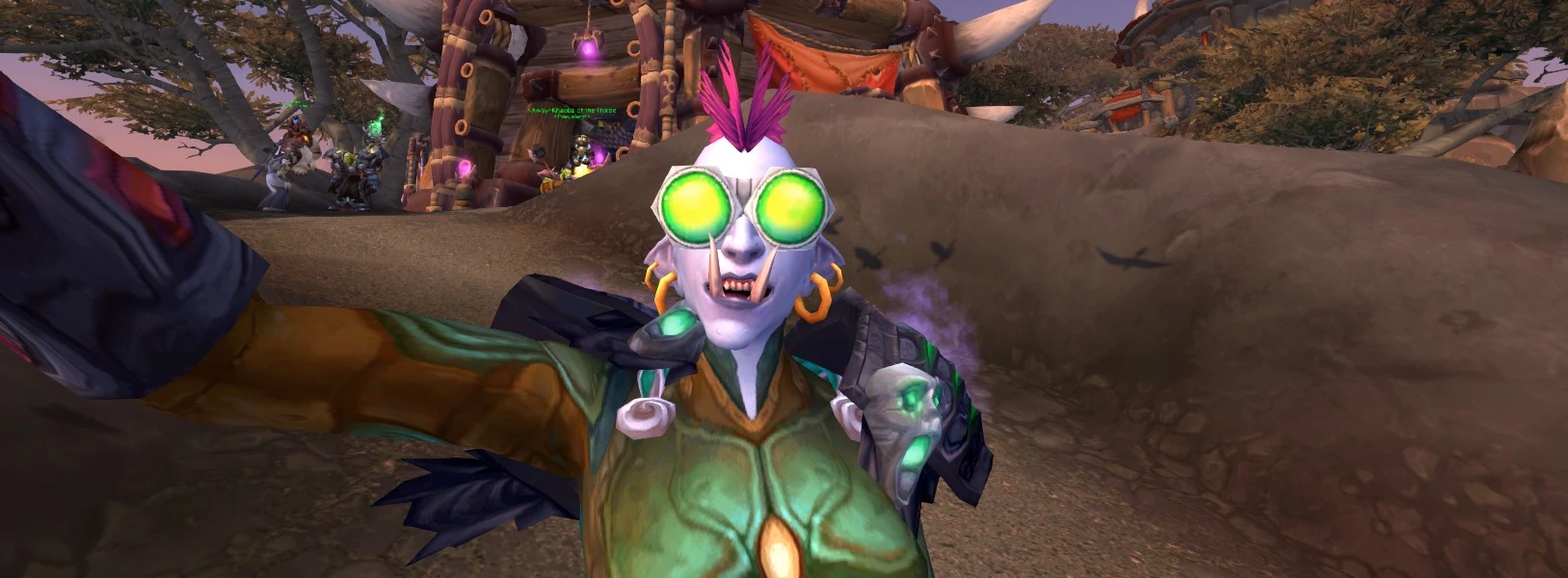 A female troll wearing bright green goggles grins with her fangs out while gazing up in an in-game selfie from World of Warcraft