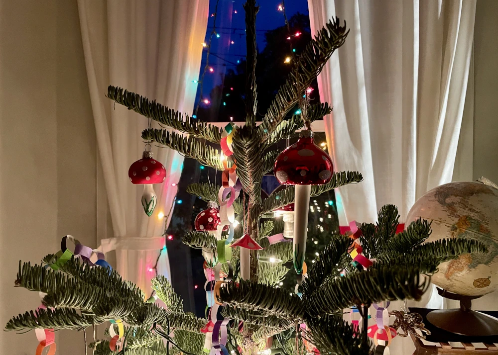 Several different kinds of mushroom ornaments on a pine tree. The mushrooms have red caps and white spots.