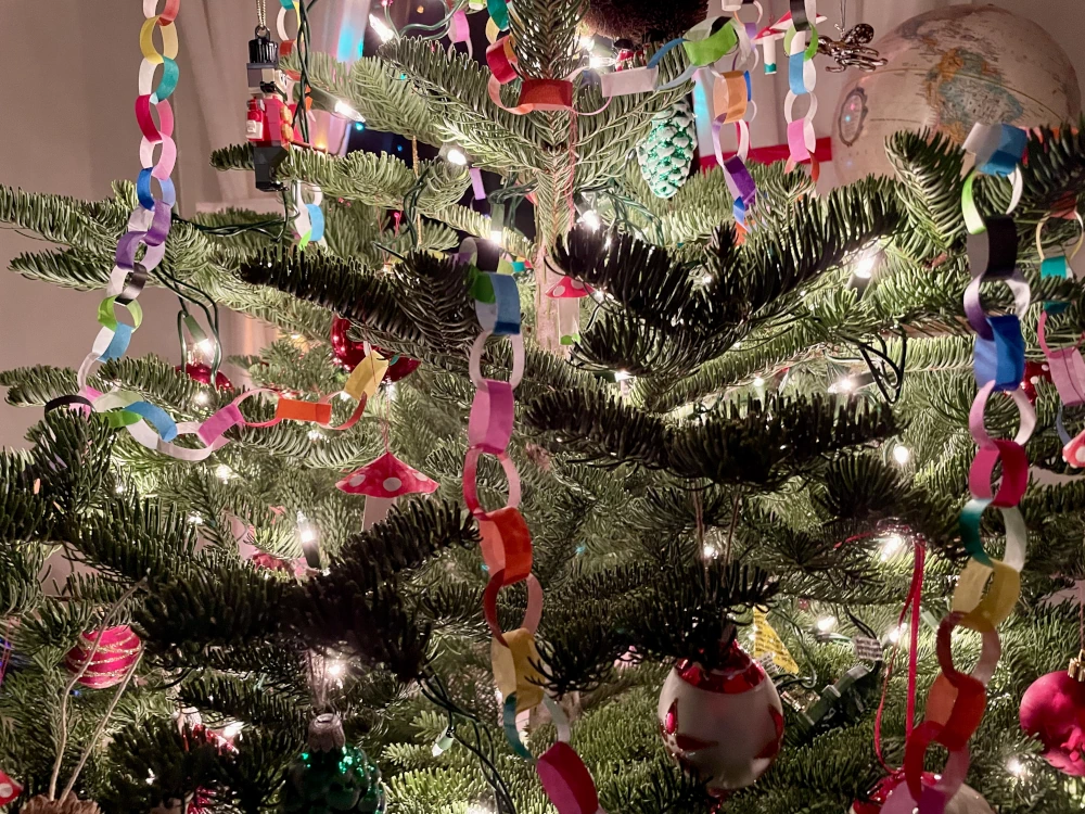 A Christmas tree with many colorful paper chains lit by the white fairly lights hung on the branches